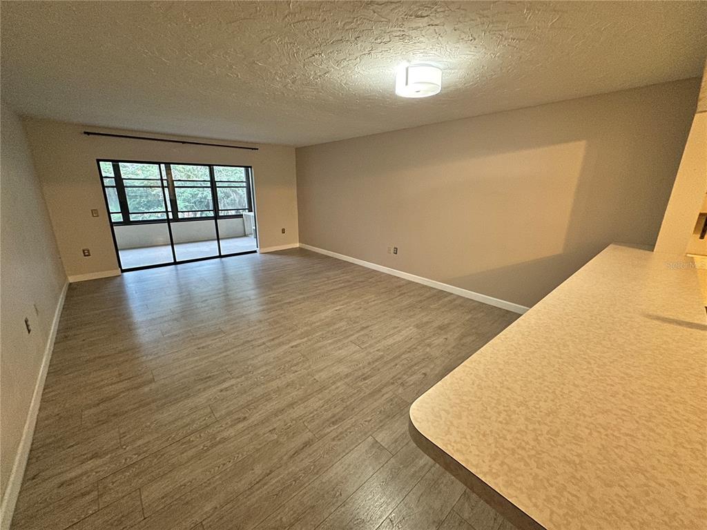 An empty living room features light wood-look flooring, beige walls, and a sliding glass door — 283 SHERWOOD DRIVE UNIT 283U, BRADENTON, FL