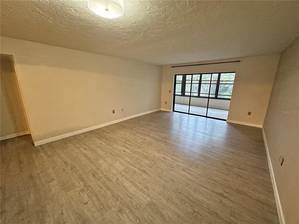 An empty living room features light wood-look flooring, beige walls, and a large sliding glass door — 283 SHERWOOD DRIVE UNIT 283U, BRADENTON, FL