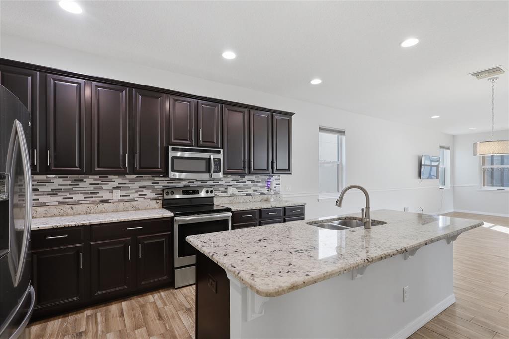 A kitchen with dark wood cabinets, granite countertops, a center island, and stainless steel appliances — 32659 HARMONY OAKS DRIVE, WESLEY CHAPEL, FL