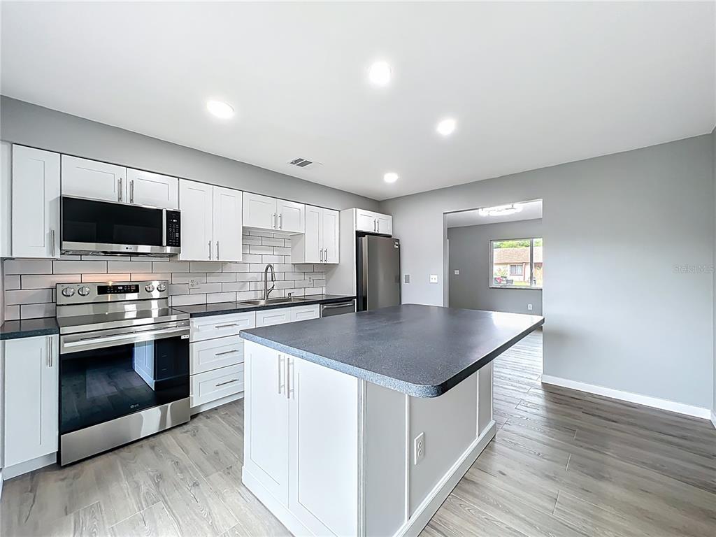 A kitchen features white cabinetry, stainless steel appliances, a center island, and gray flooring — 6848 COMPASS COURT, ORLANDO, FL