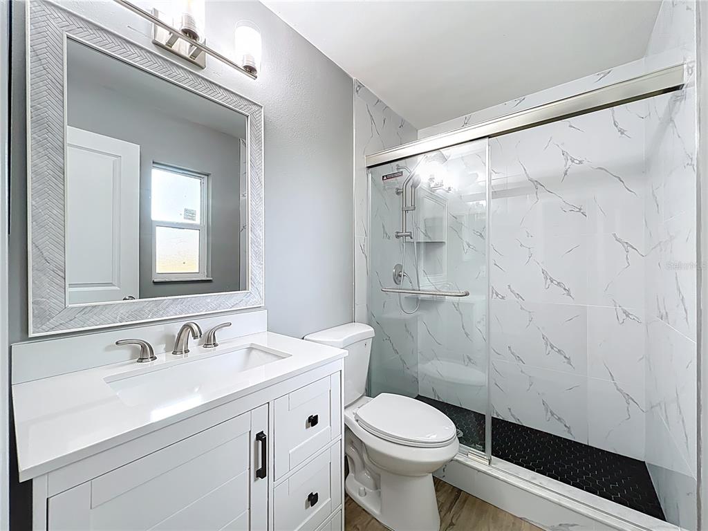 A bathroom features a white vanity, a toilet, and a glass-enclosed shower with marble-look tiles — 6848 COMPASS COURT, ORLANDO, FL
