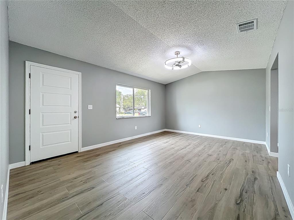 An empty room features gray walls, wood-look flooring, a popcorn ceiling, and a white door — 6848 COMPASS COURT, ORLANDO, FL