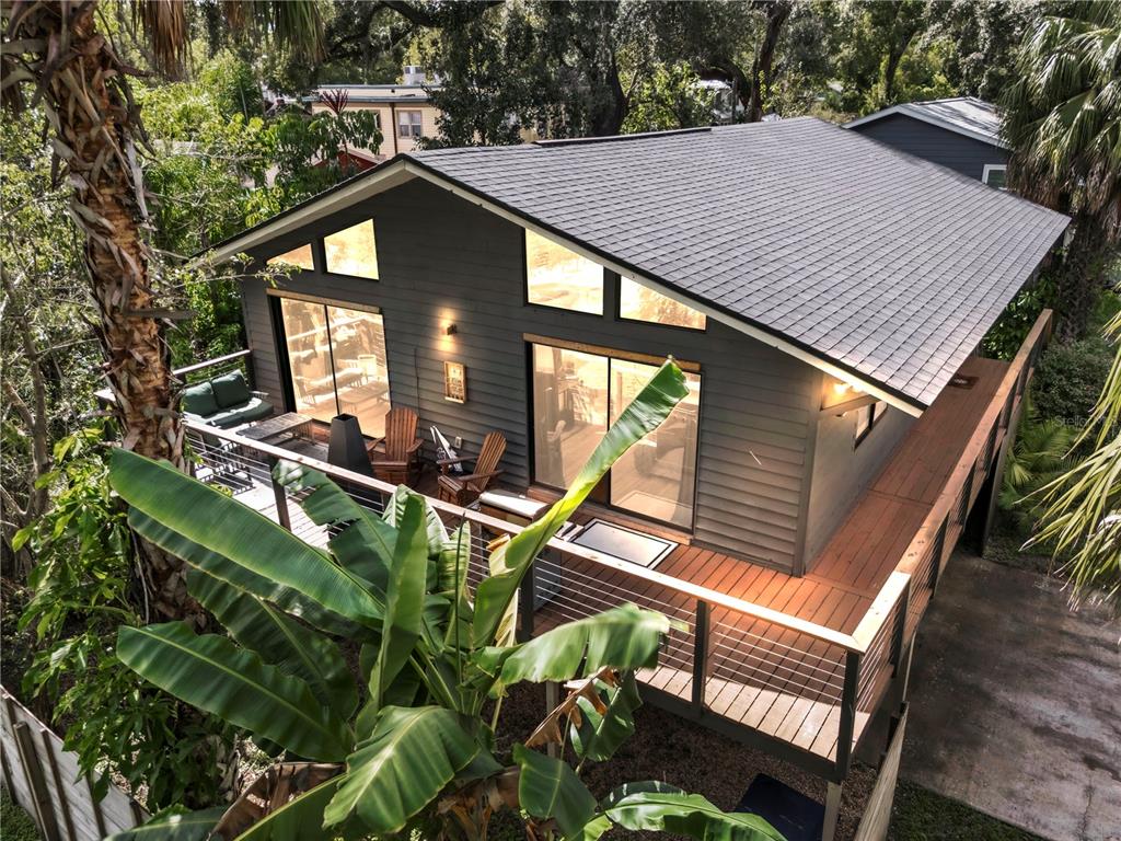 An elevated house with a large wooden deck, dark siding, and large windows among trees — 43 HAMILTON HEATH DRIVE, TAMPA, FL