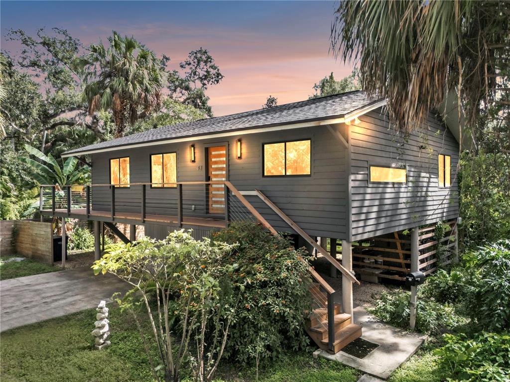 A stilted, dark gray house with a wooden deck and staircase surrounded by lush greenery — 43 HAMILTON HEATH DRIVE, TAMPA, FL