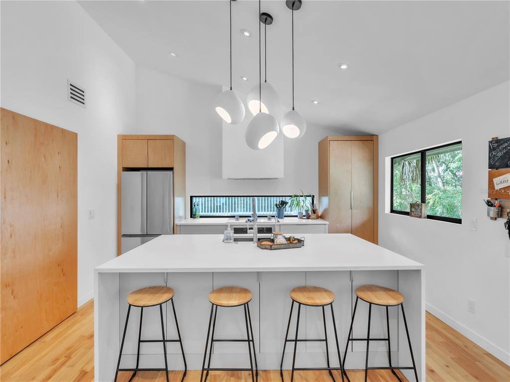 A modern kitchen features a white island with four stools, light wood cabinetry, and pendant lighting — 43 HAMILTON HEATH DRIVE, TAMPA, FL