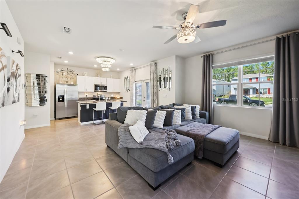 A living room with a gray sectional sofa opens to a kitchen with white cabinets — 3049 MELETO BOULEVARD, NEW SMYRNA BEACH, FL