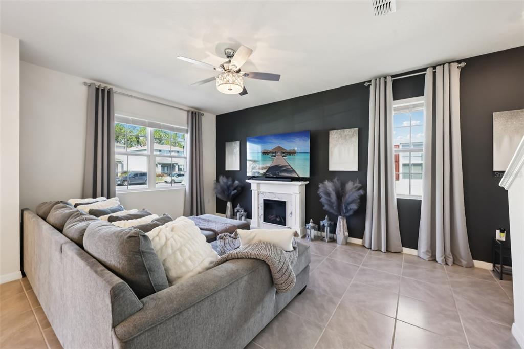 A living room features a gray sectional sofa, a fireplace with a television, and dark walls — 3049 MELETO BOULEVARD, NEW SMYRNA BEACH, FL