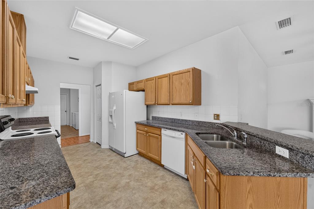 A kitchen features oak cabinets, dark granite countertops, white appliances, and a tile floor — 7852 SW 84TH WAY, GAINESVILLE, FL
