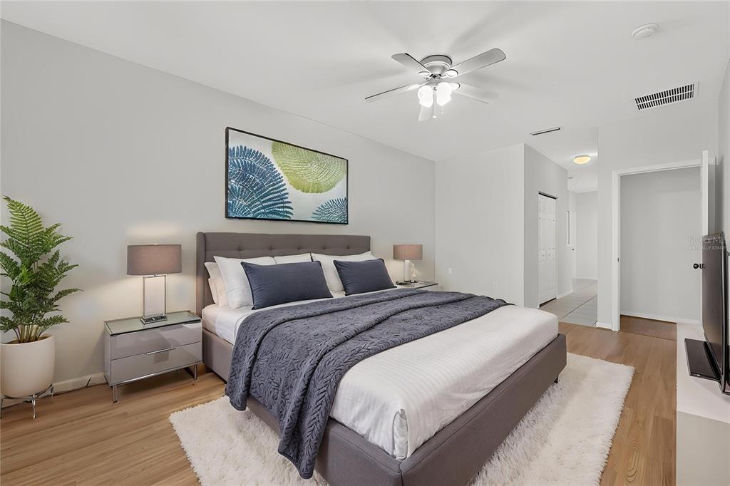 A bedroom features a gray upholstered bed, light wood flooring, and a ceiling fan — 7852 SW 84TH WAY, GAINESVILLE, FL