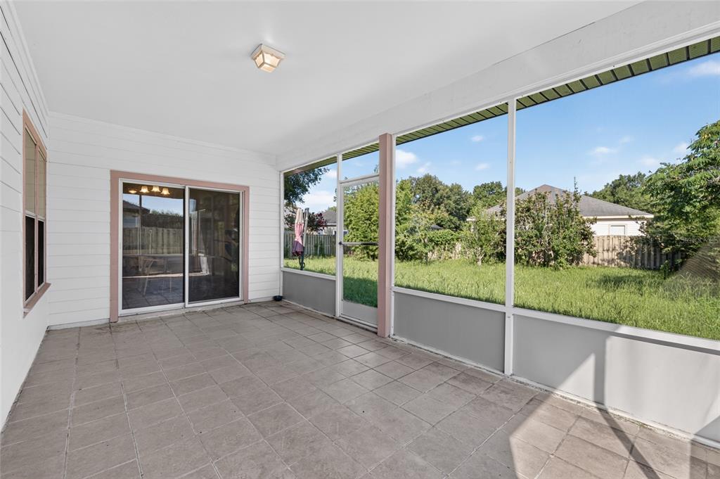 A screened-in patio features tiled flooring, white walls, and a sliding glass door — 7852 SW 84TH WAY, GAINESVILLE, FL