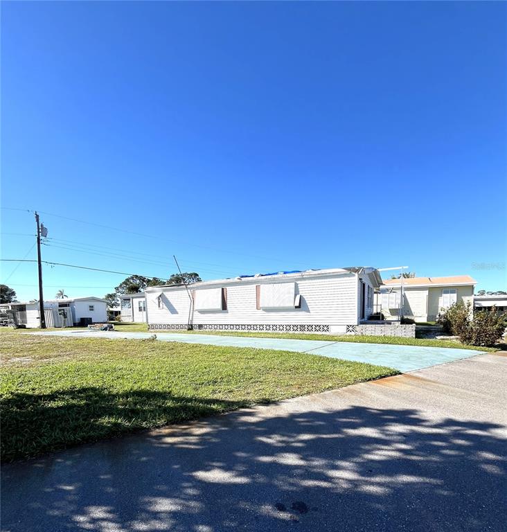 A white manufactured home with a blue tarp on the roof sits on a lot — 234 TRAILORAMA DRIVE, NORTH PORT, FL
