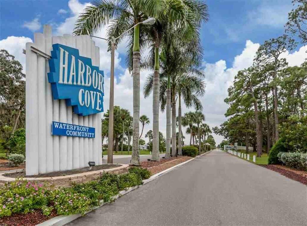 A sign for Harbor Cove Waterfront Community stands beside a paved road lined with palm trees — 234 TRAILORAMA DRIVE, NORTH PORT, FL