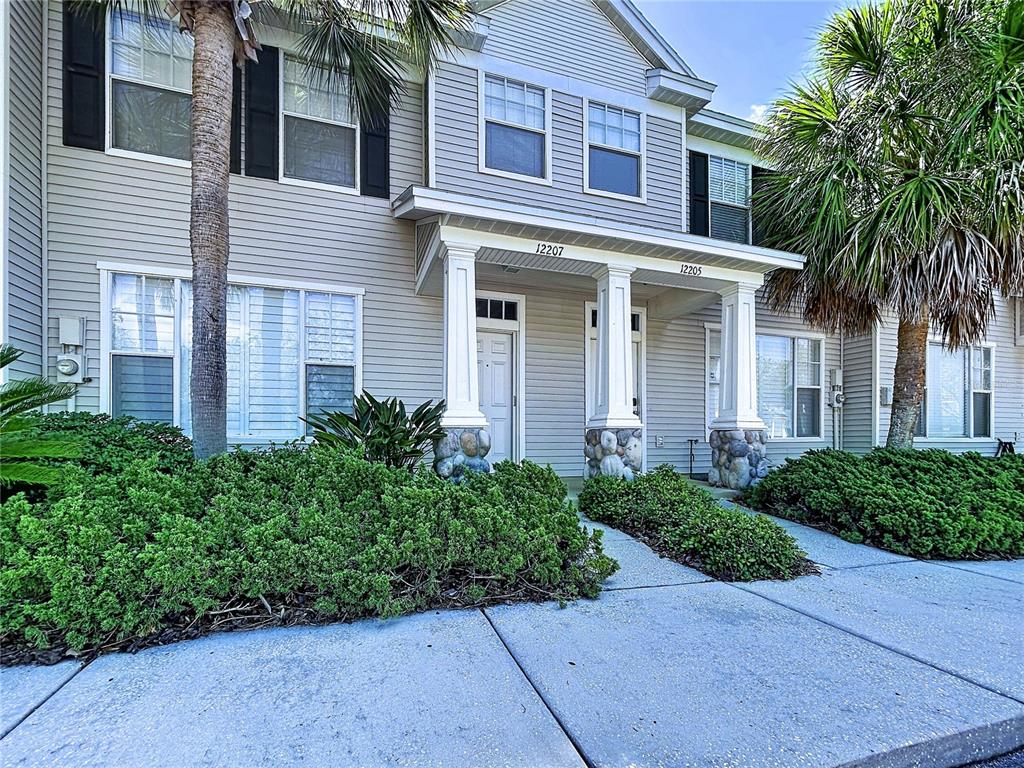 An exterior view of a two-story townhouse with light siding, palm trees, and a porch — 12207 COUNTRY WHITE CIRCLE, TAMPA, FL