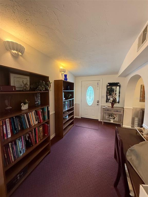 A hallway with purple carpeting, two wooden bookshelves, and a white front door — 5422 TROUBLE CREEK ROAD, NEW PORT RICHEY, FL