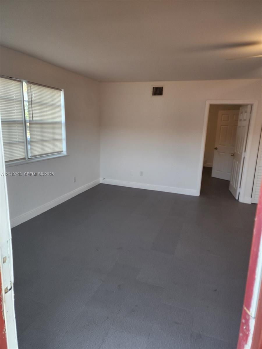 This empty room features gray flooring, white walls, a window with blinds, and a doorway — 14240 NW 22nd Ave # 3, Opa-Locka FL 33054, OPA-LOCKA, FL