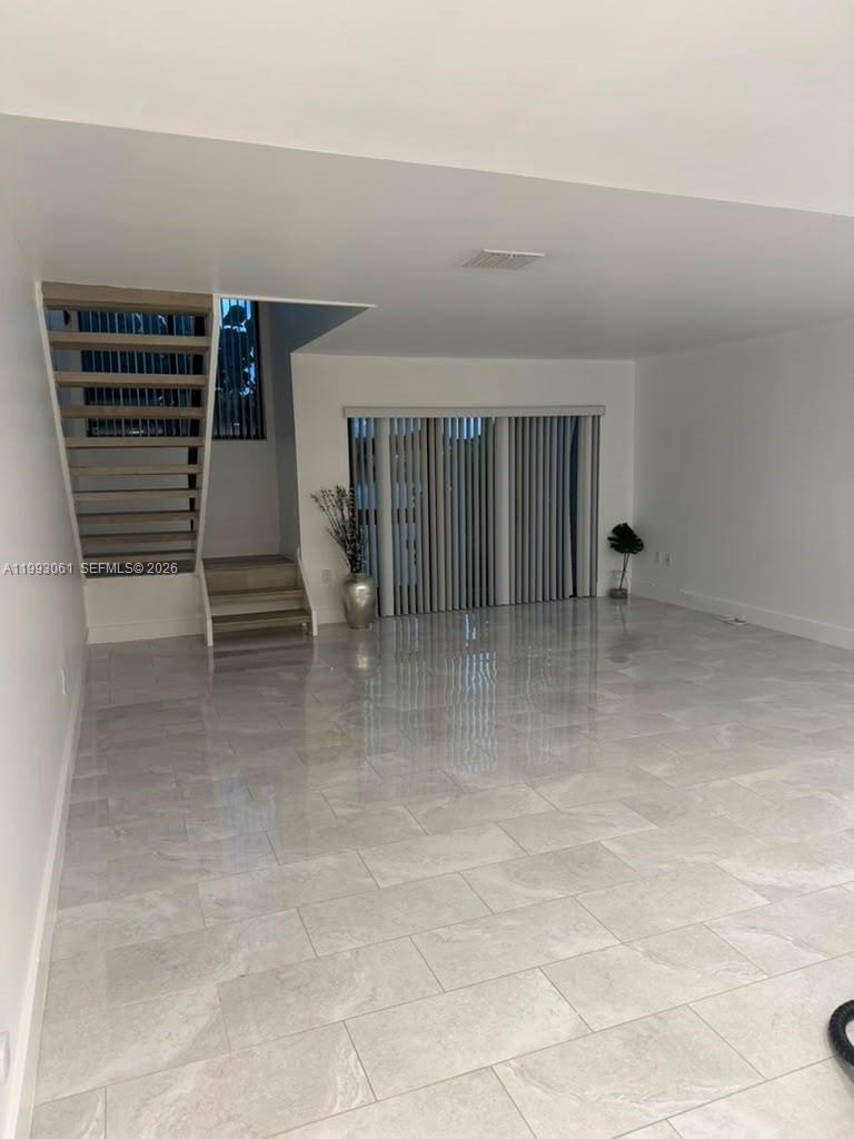 An empty room features light-colored tile flooring, a floating staircase, and vertical window blinds — 10000 NW 9th St Cir # 11, Miami FL 33172, MIAMI, FL