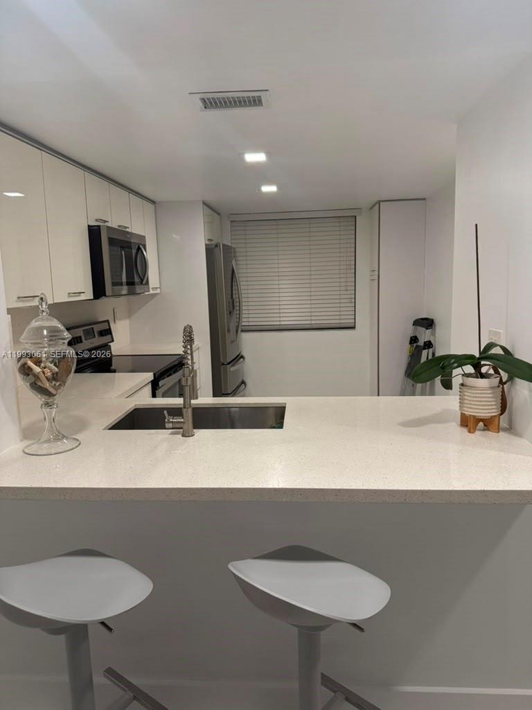 A modern kitchen features white cabinetry, quartz countertops, stainless steel appliances, and a breakfast bar — 10000 NW 9th St Cir # 11, Miami FL 33172, MIAMI, FL