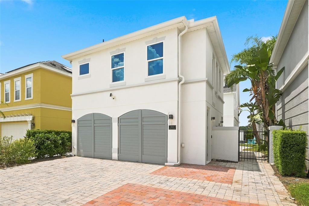 A two-story white house with two gray arched garage doors and a brick driveway — 1530 COROLLA COURT, REUNION, FL