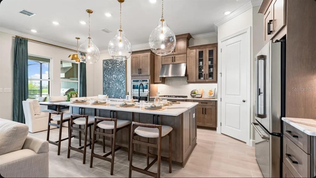 A kitchen features a large island with bar seating, wooden cabinetry, and glass pendant lights — 7636 MOONBEAM AVENUE, SARASOTA, FL