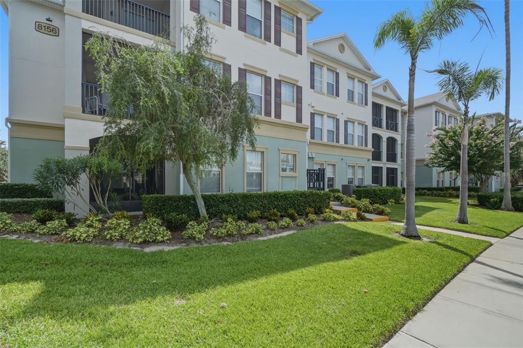 A multi-story apartment building with light-colored siding, dark shutters, and a landscaped lawn — 8156 BOAT HOOK LOOP UNIT 109, WINDERMERE, FL