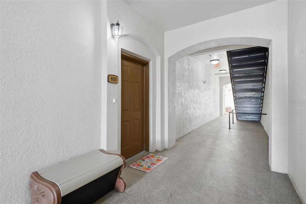 An apartment building hallway features a brown door labeled 602, a bench, and stairs — 8156 BOAT HOOK LOOP UNIT 109, WINDERMERE, FL