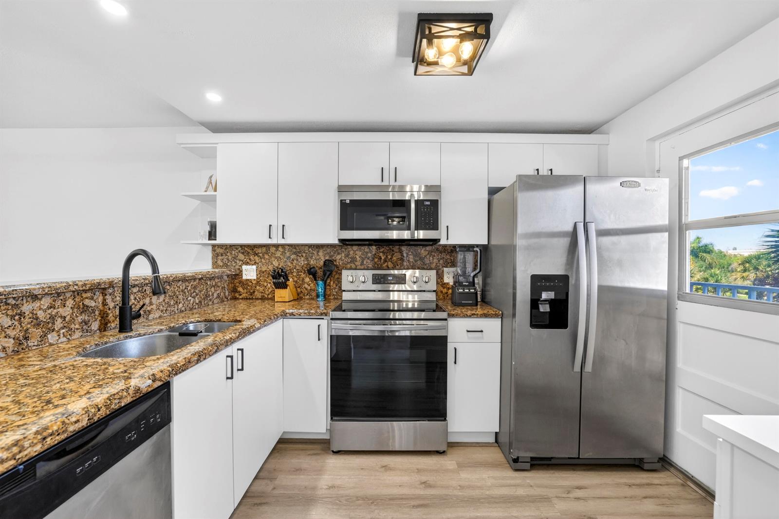 A kitchen features white cabinets, granite countertops, stainless steel appliances, and wood-look flooring — 5961 NW 2nd Avenue # 302, Boca Raton FL 33487, BOCA RATON, FL