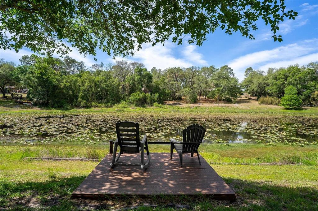 Two dark chairs sit on a wooden deck overlooking a pond filled with lily pads — 4024 EAGLE RIDGE ROAD, FRUITLAND PARK, FL