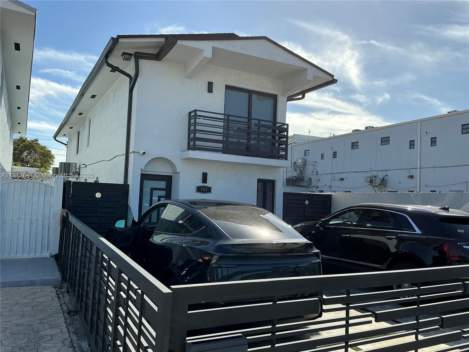 A two-story white house features a balcony, dark trim, and a fenced driveway with cars — 717 Tamiami Canal Rd, Miami FL 33144, MIAMI, FL