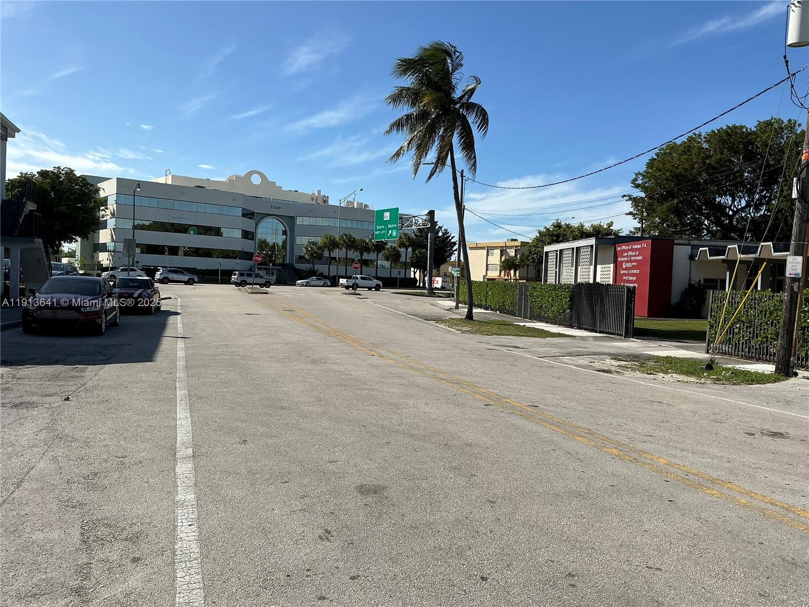 A street view shows a paved road leading toward a large office building under blue skies — 717 Tamiami Canal Rd, Miami FL 33144, MIAMI, FL