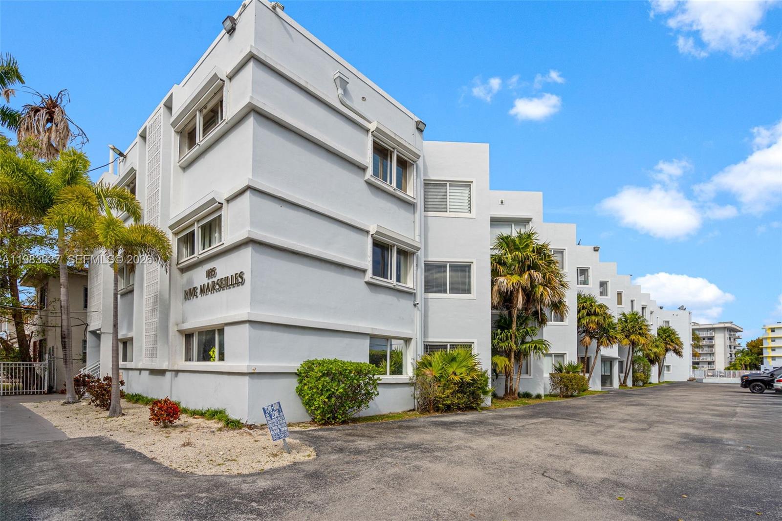 A multi-story white apartment building with palm trees and a paved parking area — 1185 Marseille Dr # 202, Miami Beach FL 33141, MIAMI BEACH, FL