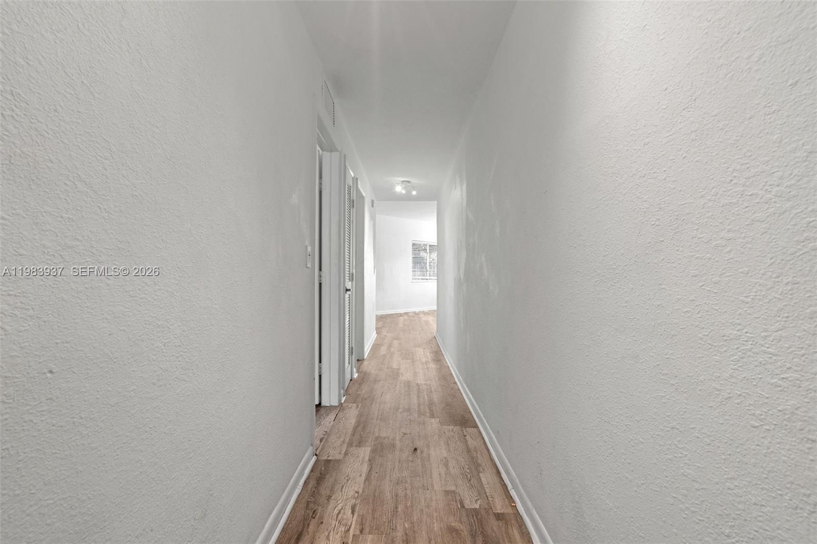 A narrow hallway features white walls, wood-look flooring, and a doorway leading to another room — 1185 Marseille Dr # 202, Miami Beach FL 33141, MIAMI BEACH, FL