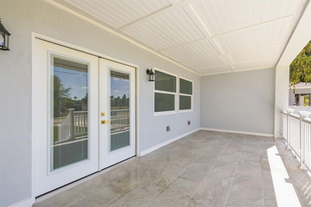 A covered patio features light gray walls, tiled flooring, white French doors, and a white railing — 6510 E 23RD AVENUE, TAMPA, FL