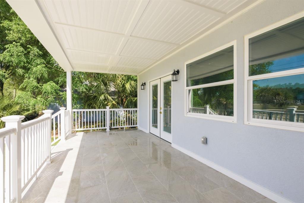 A covered patio features light-colored tile flooring, white railings, and glass double doors — 6510 E 23RD AVENUE, TAMPA, FL