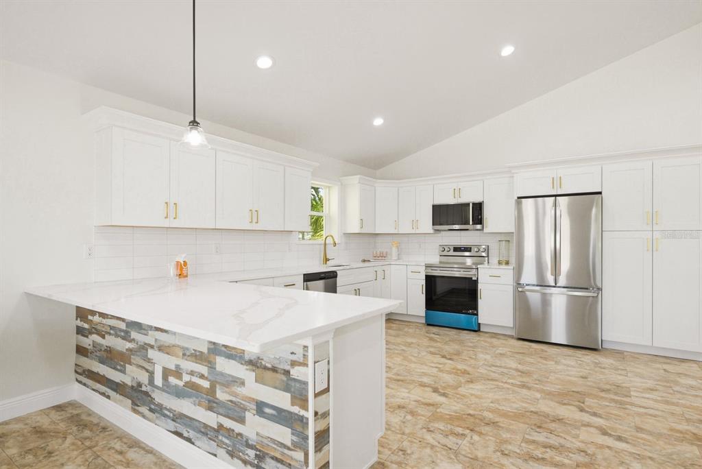 A kitchen features white cabinets, stainless steel appliances, a quartz island, and wood-look tile flooring — 6510 E 23RD AVENUE, TAMPA, FL