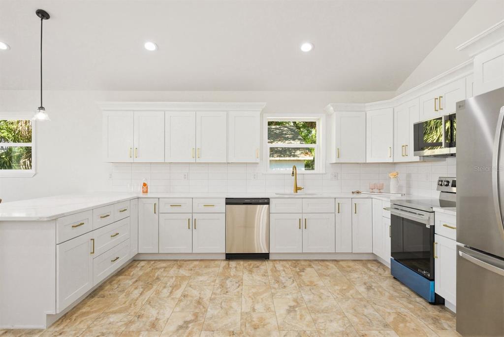 A kitchen features white cabinets, stainless steel appliances, a gold faucet, and light tile flooring — 6510 E 23RD AVENUE, TAMPA, FL