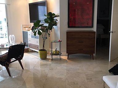 A living room features a wooden dresser, a television, a potted plant, and tiled flooring — 888 Brickell Key Dr # 600, Miami FL 33131, MIAMI, FL