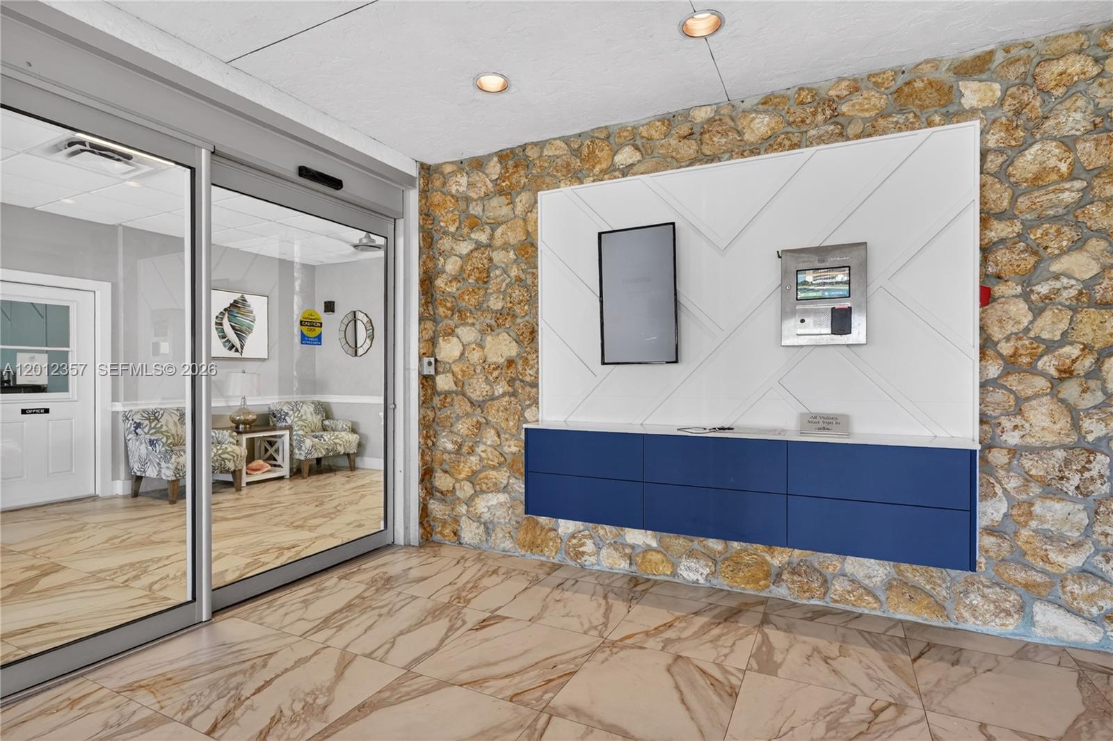 A lobby features a stone wall, a blue floating cabinet, and a glass-enclosed office area — 5 Bluebill # 201, Naples FL 34108, NAPLES, FL