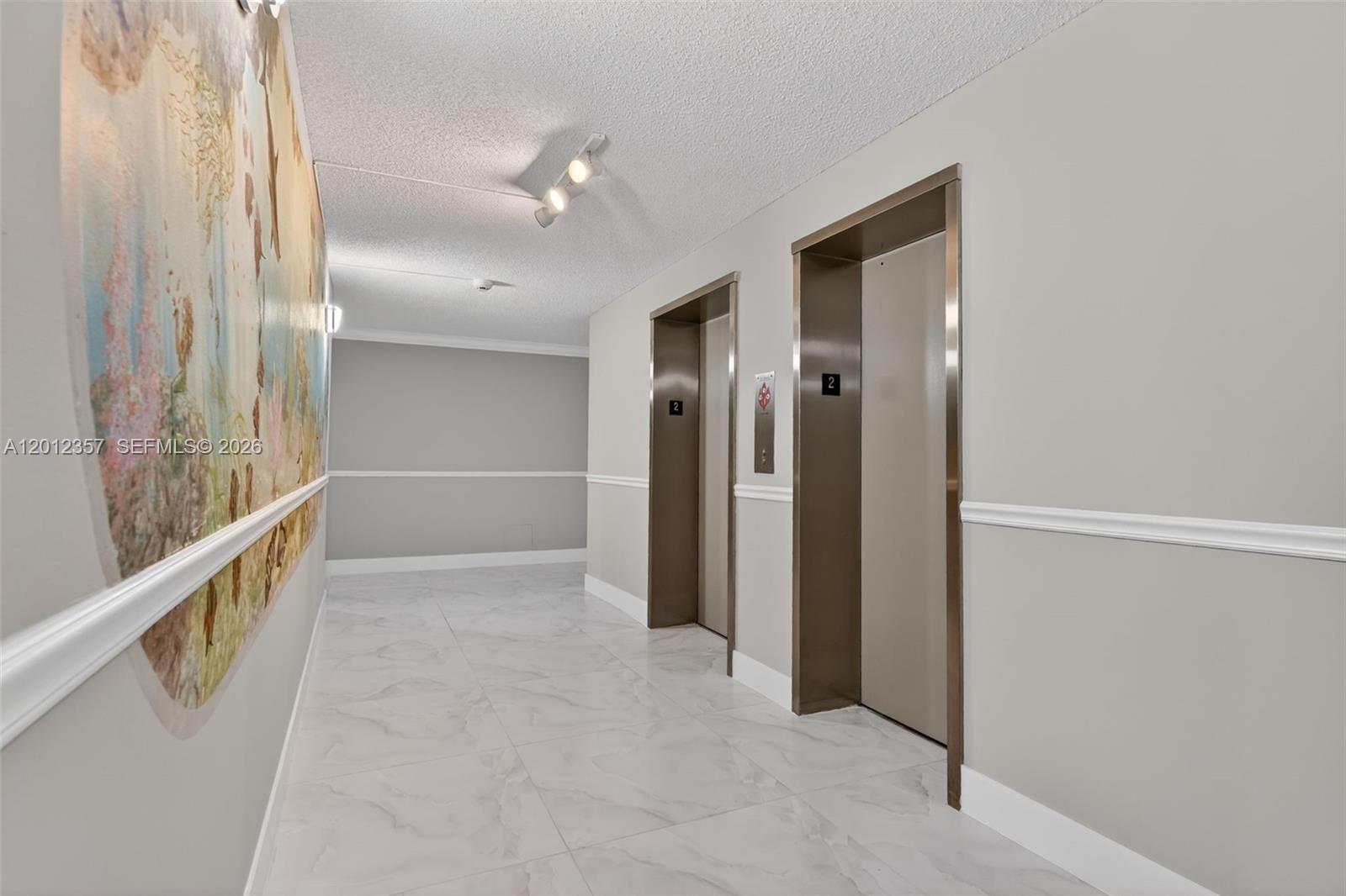 An elevator lobby features two metallic elevator doors, light-colored tile flooring, and a wall mural — 5 Bluebill # 201, Naples FL 34108, NAPLES, FL