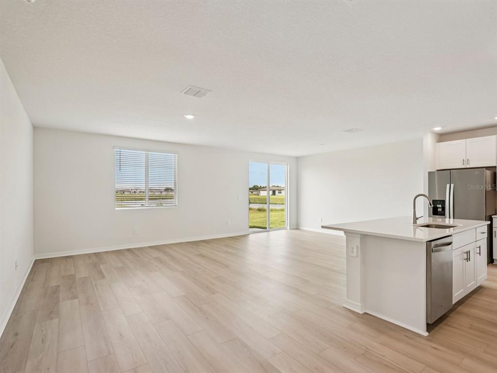 An open-concept living area features light wood-look flooring, white walls, and a modern kitchen island — 10432 ABUNDANCE GROVE WAY, PARRISH, FL