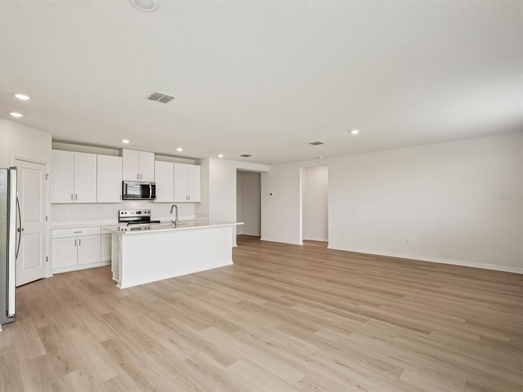 An open-concept kitchen features white cabinets, a central island, and light wood-look flooring — 10432 ABUNDANCE GROVE WAY, PARRISH, FL