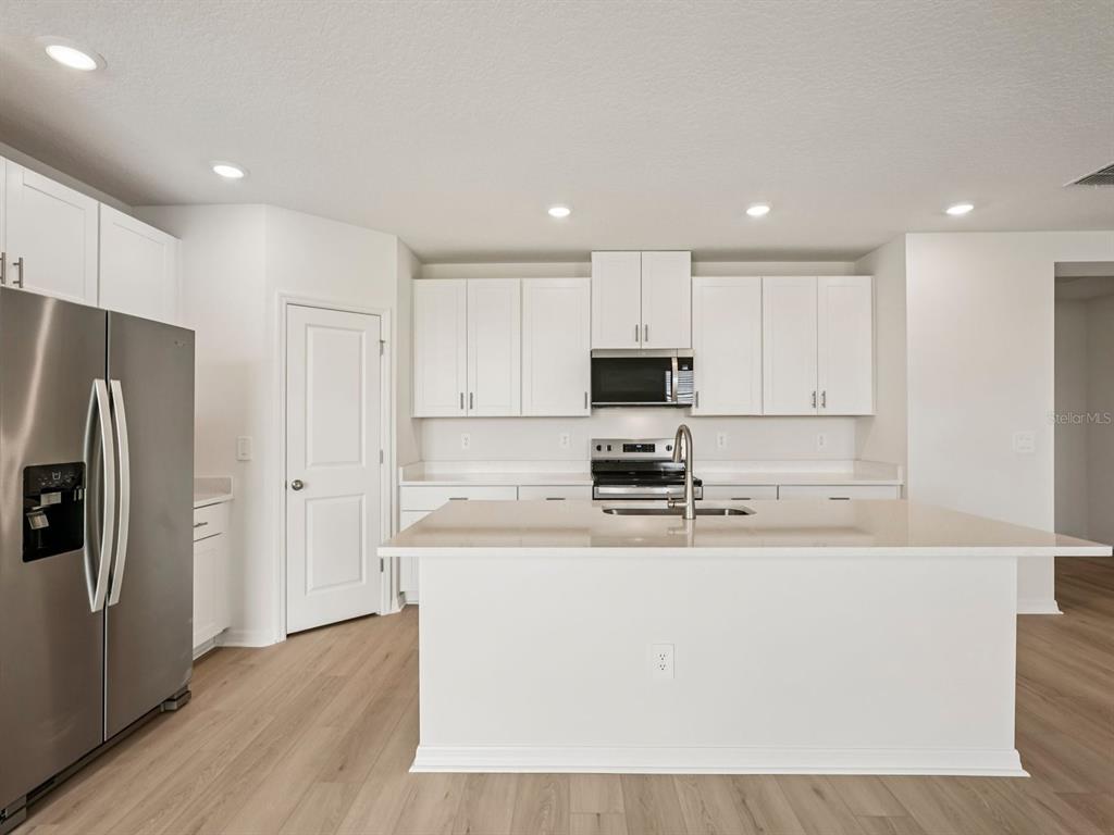 A modern kitchen features white cabinets, stainless steel appliances, and a large central island — 10432 ABUNDANCE GROVE WAY, PARRISH, FL