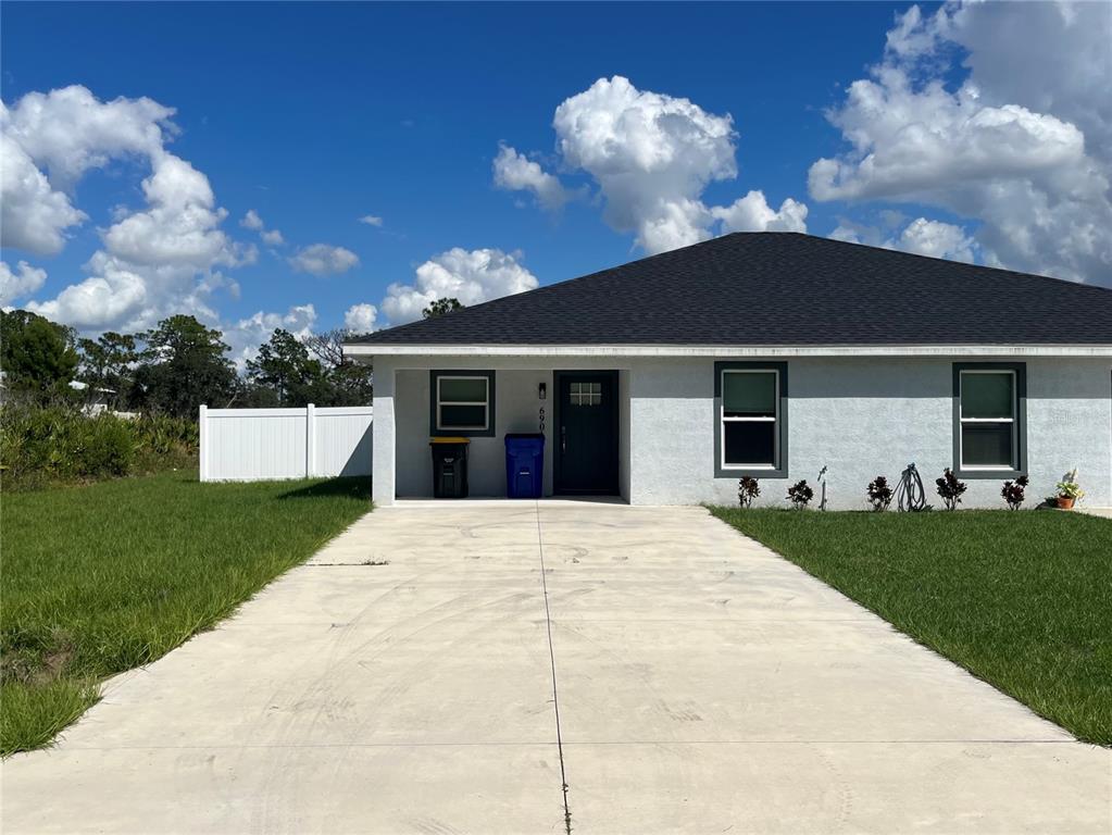 A single-story house with a concrete driveway, white stucco exterior, and a dark roof — 7056 SAN BENITO DRIVE, SEBRING, FL