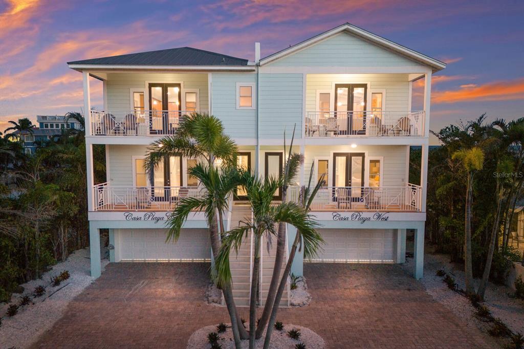 An exterior view of a two-story duplex house with balconies and palm trees at sunset — 105 4TH STREET S, BRADENTON BEACH, FL