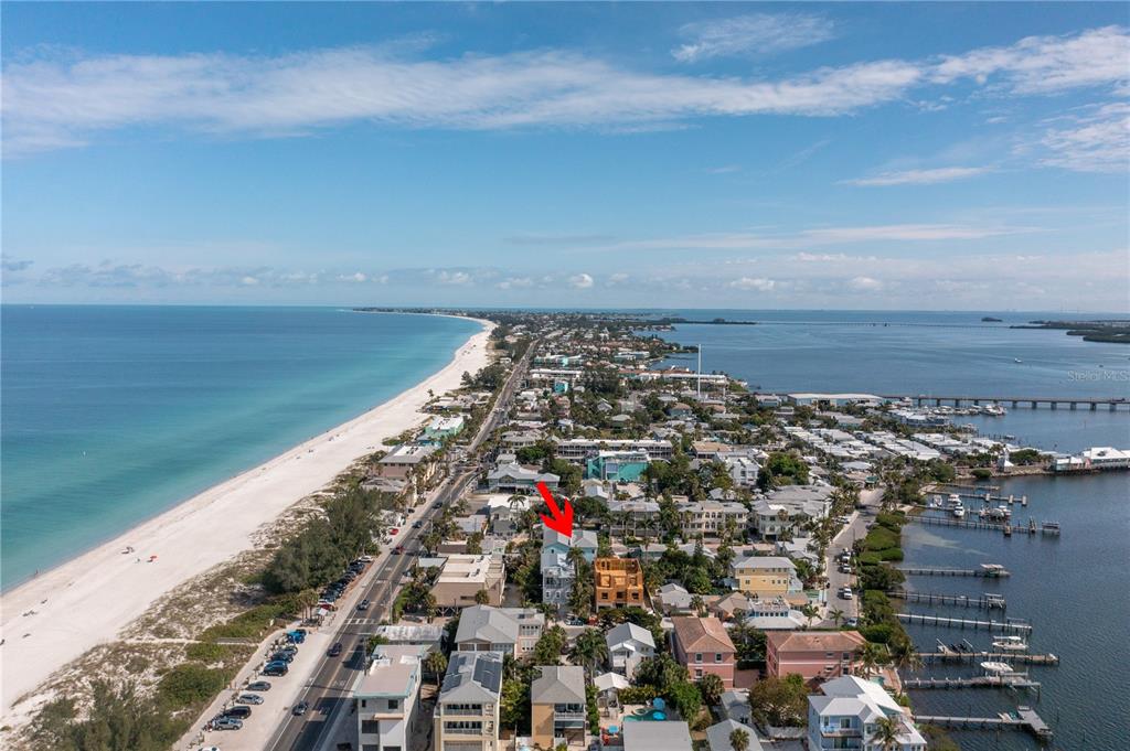 An aerial view shows a coastal town with a red arrow pointing to a specific house — 105 4TH STREET S, BRADENTON BEACH, FL