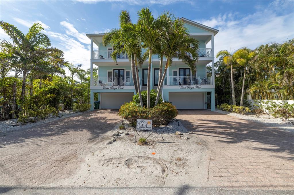 A three-story light blue duplex with two garage bays and palm trees in the front — 105 4TH STREET S, BRADENTON BEACH, FL