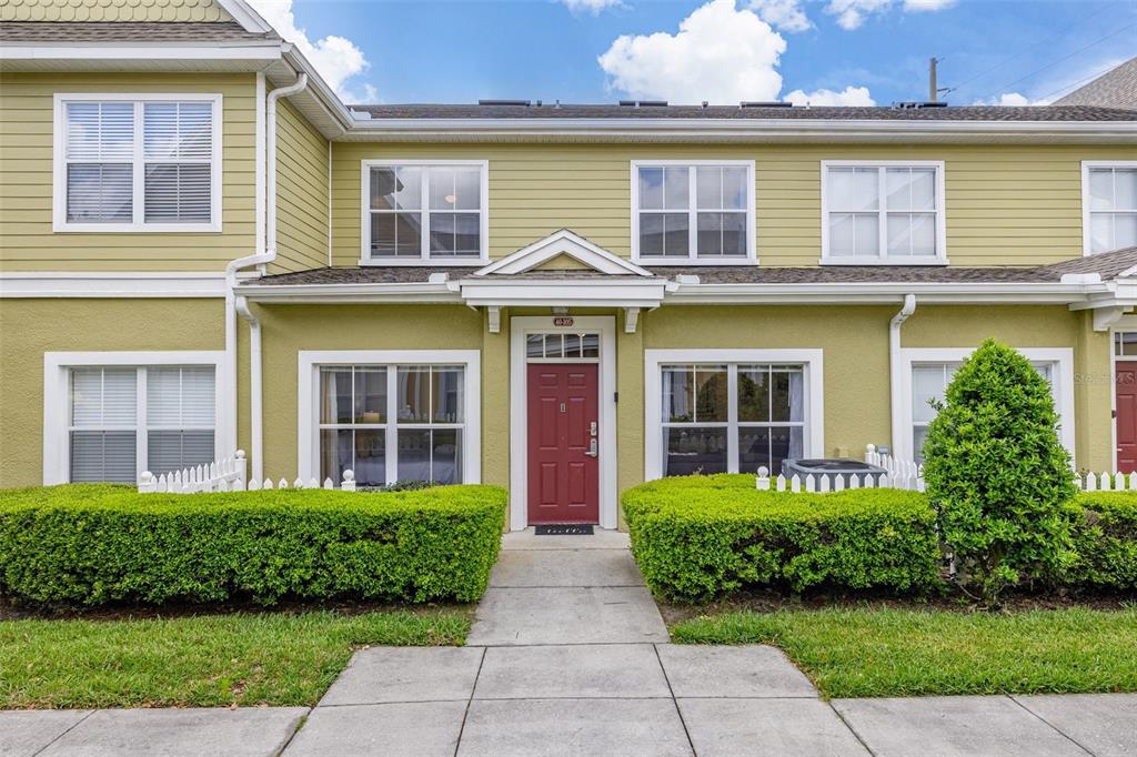 A two-story townhouse exterior with light green siding, a red front door, and manicured hedges — 2250 SAN VITAL DRIVE UNIT 105, KISSIMMEE, FL