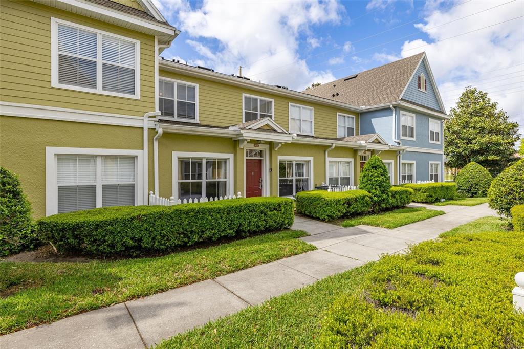A multi-story townhouse exterior with yellow and blue siding, a red door, and manicured hedges — 2250 SAN VITAL DRIVE UNIT 105, KISSIMMEE, FL