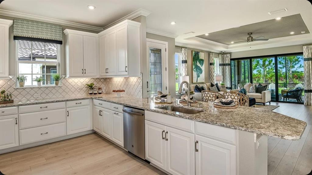 A kitchen with white cabinets, granite countertops, and a stainless steel dishwasher overlooks a living area — 14509 DERNA TERRACE, BRADENTON, FL