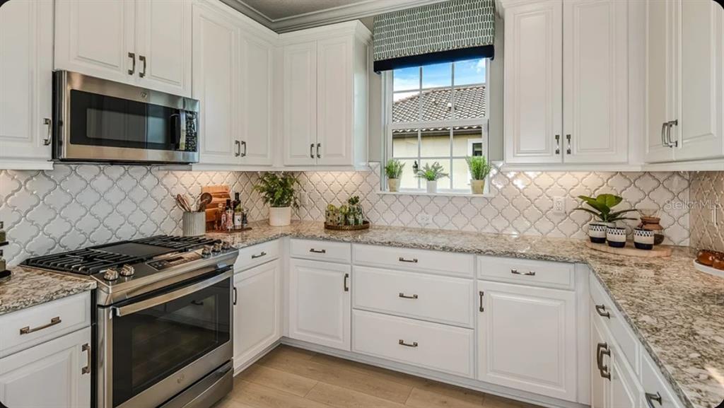 A kitchen with white cabinets, granite countertops, stainless steel appliances, and a patterned tile backsplash — 14509 DERNA TERRACE, BRADENTON, FL