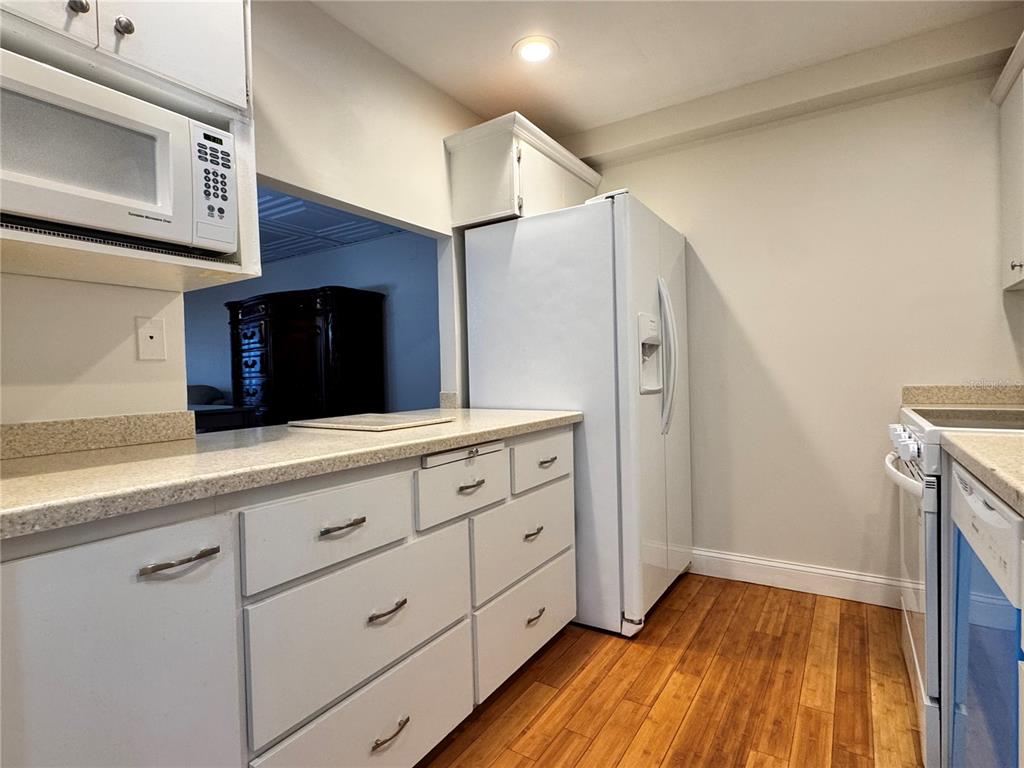 A kitchen features white cabinets, a white refrigerator, a microwave, and light-colored countertops — 3255 RAMBLEWOOD PLACE, SARASOTA, FL